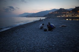 Iranian refugees are breaking their fast during Ramadan on the beach in Ventimiglia, Italy. In the distance is France. July 2015.